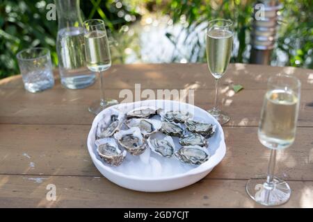 Un gros plan d'huîtres fraîches ouvertes et de coquillages avec des quartiers de citron, deux verres de vin blanc ou de champagne sur une table extérieure Banque D'Images