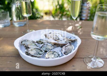 Un gros plan d'huîtres fraîches ouvertes et de coquillages avec des quartiers de citron, deux verres de vin blanc ou de champagne sur une table extérieure Banque D'Images