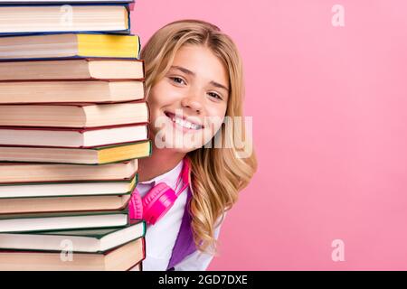 Portrait d'une jolie fille gaie se cachant derrière l'espace de copie de livre de pile isolé sur fond rose pastel couleur Banque D'Images