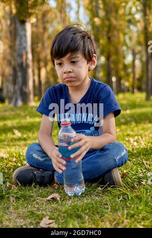 Brunette enfant pensivement tenant une petite bouteille d'eau assis au milieu de la forêt à l'automne. Vertical, arrière-plan flou Banque D'Images