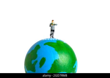 Photographie miniature de personnage de jouet de personnes. Journée de lecture internationale ou nationale. Un étudiant homme se tenant au-dessus du globe terrestre tout en lisant un livre, isolé o Banque D'Images