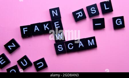 Un groupe de mosaïque scarable formant le mot escroquerie fausses nouvelles. Mise au point sélective sur les tuiles isolées sur fond rose Banque D'Images