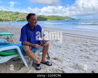 10 août 2021, Thaïlande, Patong: Hardy Wutke, chauffeur de train de Berlin, est assis sur son chaise longue sur la plage vide de Patong. L'homme de 57 ans participe au projet modèle « boîte à lettres » pour se réunir avec son ami Watt, avec qui il travaille depuis 17 ans. Le 1er juillet, la plus grande île de Thaïlande a lancé son très attendu projet modèle Corona 'Sandbox' pour revitaliser le tourisme. Depuis lors, Phuket est devenu l'une des rares destinations long-courriers au monde où les personnes de près de 70 pays peuvent passer des vacances sans quarantaine, tant qu'elles sont pleinement vaccinées. Photo: Carola Frentzen/dpa Banque D'Images