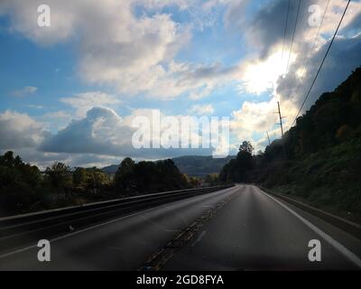 Capturant la beauté sereine d'une pause ensoleillée à travers un ciel nuageux, cette photo vous invite à un voyage visuel sur une route sinueuse, encadrée par roulis Banque D'Images