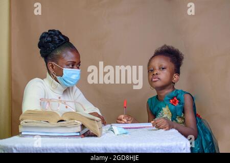 Une enseignante ou une mère africaine avec masque nasal, enseignant et aidant une petite fille avec ses études à exceller dans l'école, l'éducation et la carrière Banque D'Images