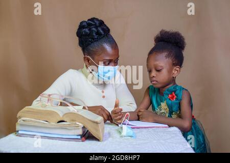 Une enseignante ou une mère africaine avec masque nasal, enseignant et aidant une petite fille avec ses études à exceller dans l'école, l'éducation et la carrière Banque D'Images