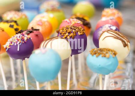 Un assortiment coloré de gâteaux pop, magnifiquement décorés avec des pépites, du filet de chocolat et des revêtements vibrants, affichés sur des bâtons. Banque D'Images