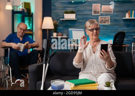 Couple retraité mature sur appel vidéo moderne à la maison à l'aide de la technologie smartphone de conférence en ligne. Homme aîné lisant pendant que la femme senior parle à la famille sur la connexion Internet webcam Banque D'Images