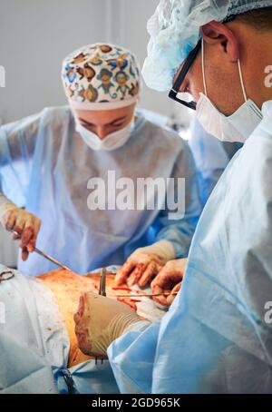 Médecins effectuant la chirurgie de l'abdominoplastie en clinique. Concentrez-vous sur le chirurgien plastique masculin effectuant une chirurgie plastique abdominale en salle d'opération. Concept de Banque D'Images