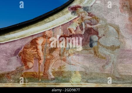 Des fresques décolorées attribuées au peintre de l'église Josef Anton Puellacher (1737-1799) décorent le pignon gracieux de l'Ortskapelle sur le bord de la route baroque ou la chapelle locale de Fronhausen sur le plateau Mieming ou Mieminger, une terrasse de montagne jusqu'à 1,000 m (3,280 pi) au-dessus de la vallée de l'auberge supérieure dans le Nord Tyrol, en Autriche. Les œuvres d'art, au-dessous d'un bellcote à bois, incluent cette représentation de Saint Martin de Tours qui divise son manteau avec un mendiant. Banque D'Images