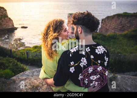 Les jeunes couples hétérosexuels s'embrassent au sommet d'une falaise près de l'océan. Banque D'Images