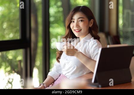 Femme d'affaires dans un ensemble formel de boire du café devant l'ordinateur portable, détendu avec un bon café et de la verdure vue extérieure Banque D'Images
