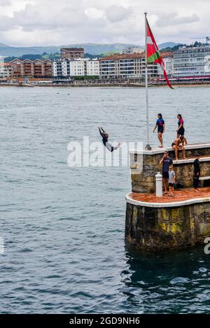 Zarautz, Espagne - 25 juillet 2021 : les adolescents de la région sautent dans la mer depuis les murs du port de la ville de Zarautz, dans le pays Basque Banque D'Images