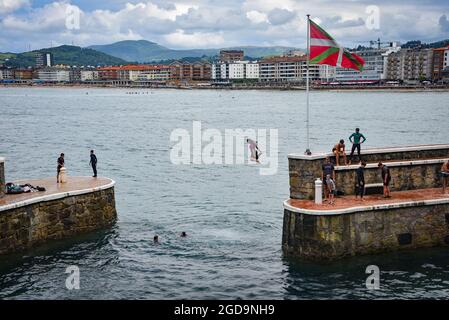 Zarautz, Espagne - 25 juillet 2021 : les adolescents de la région sautent dans la mer depuis les murs du port de la ville de Zarautz, dans le pays Basque Banque D'Images