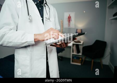 Infirmière de sexe masculin debout en clinique, dactylographiant sur une tablette numérique Banque D'Images