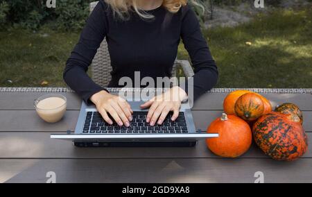 Les mains des femmes travaillent sur un ordinateur portable. À côté du clavier se trouve une tasse de cappuccino et de petits citrouilles orange. Travail à domicile, enseignement à distance, freelance. A Banque D'Images