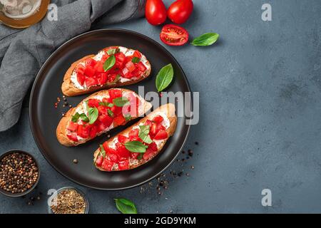 Bruschetta à la tomate, au fromage et au basilic dans une assiette noire. Hors-d'œuvre italien. Banque D'Images