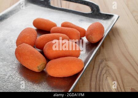 Plusieurs mini carottes mûres et biologiques sur un plateau en métal, gros plan, sur une table en bois. Banque D'Images