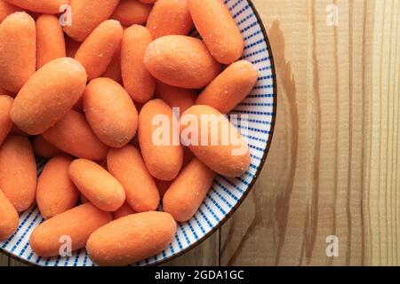 Mini carottes pelées, juteuses d'orange vif sur des plats en céramique, gros plan, sur une table en bois, vue du dessus. Banque D'Images