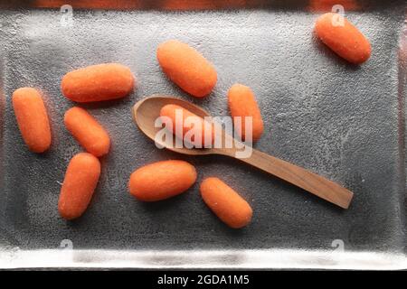 Plusieurs mini carottes orange vif sur un plateau en métal avec une cuillère en bois, gros plan, vue du dessus. Banque D'Images