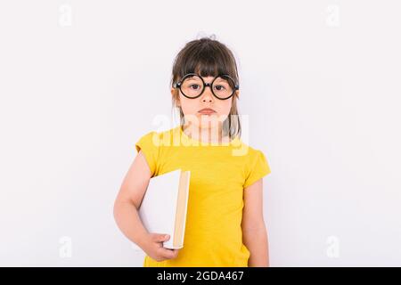 Petite fille avec un geste sérieux portant un t-shirt jaune et des verres noirs ronds tenant un papier blanc dans une main sur fond blanc Banque D'Images