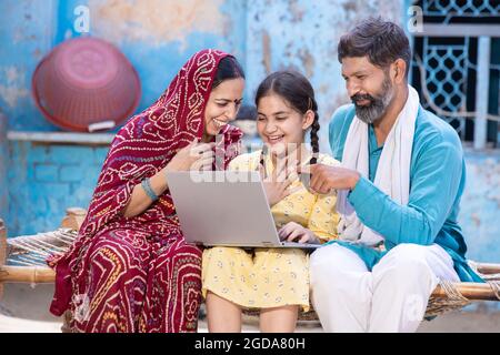 Une petite fille indienne heureuse utilisant un ordinateur portable tout en étant assise avec son père et sa mère. Les parents de village motivent le soutien de leur fille pour l'educa en ligne Banque D'Images