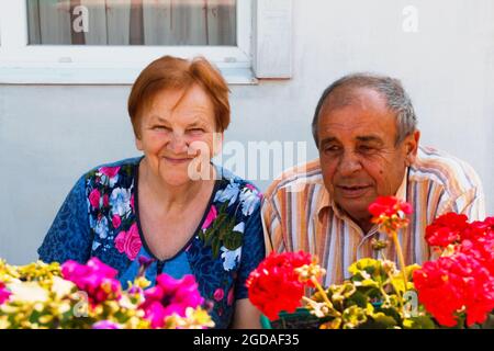 Couple âgé souriant en été. Joyeux couple de personnes âgées de mari et de femme assis sur le jardin de fleurs arrière-plan. Amour et concept de famille. Banque D'Images