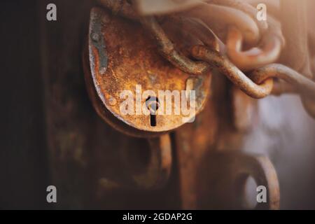 Un grand cadenas rouillé et une chaîne en métal rouillé ferment la vieille porte, éclairée par la lumière du soleil. Secret. Banque D'Images
