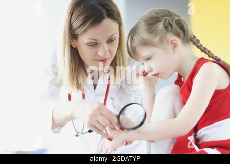 Médecin examinant la peau sur la main de la petite fille en utilisant la loupe en clinique Banque D'Images