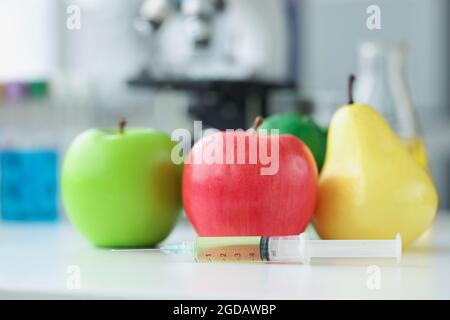 Les pommes et les poires sont allongés sur la table en laboratoire près de la seringue avec un médicament de gros plan Banque D'Images