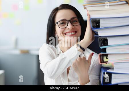 Jeune femme avec des lunettes tenant beaucoup de dossiers avec des documents dans le bureau Banque D'Images