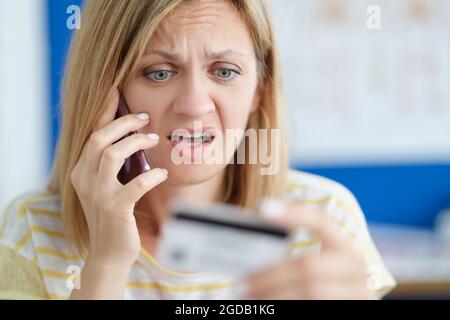 Surprise contrariée femme parlant sur téléphone mobile et tenant la carte bancaire Banque D'Images