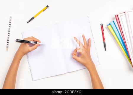 Enfant tenant un crayon dans la main gauche pour écrire dans un carnet, faire des devoirs. Signe de geste de la main OK, OK, oui. Vue de dessus. Jour des gauchers Banque D'Images