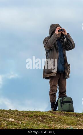 homme observation des oiseaux debout sur la plage regardant à travers une paire de jumelles, twitcher sur la côte de norfolk, ornithologue à l'aide de jumelles, snettisham. Banque D'Images