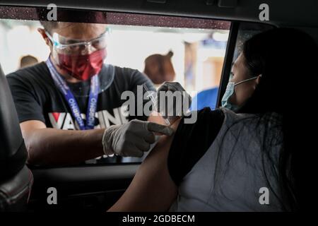 Une femme reçoit une injection du vaccin Pfizer COVID-19 sur un site de vaccination au drive lors d'un confinement plus strict à Manille. Des milliers de personnes se sont enferlées dans les centres de vaccination contre le coronavirus de la capitale philippine, défiant ainsi les restrictions de distanciation sociale, après la propagation de fausses nouvelles selon lesquelles les résidents non vaccinés seraient privés d'aide financière ou empêchés de quitter leur domicile au cours d'un confinement de deux semaines. Philippines. Banque D'Images