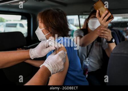 Vendredi, une femme reçoit une injection du vaccin Pfizer COVID-19 sur un site de vaccination au drive-in, lors d'un confinement plus strict à Manille, aux Philippines. 6 août 2021. Des milliers de personnes se sont enferlées dans les centres de vaccination contre le coronavirus de la capitale philippine, défiant ainsi les restrictions de distanciation sociale, après la propagation de fausses nouvelles selon lesquelles les résidents non vaccinés seraient privés d'aide financière ou empêchés de quitter leur domicile au cours d'un confinement de deux semaines. Banque D'Images