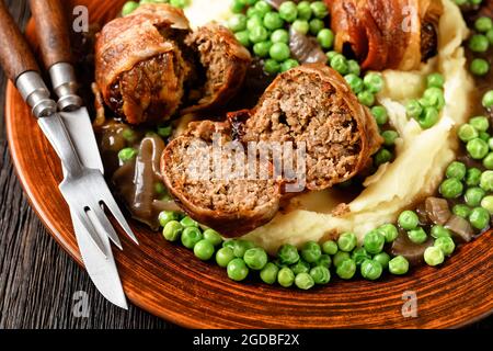 gros plan de faggots cuits servis avec une purée de pommes de terre crémeuse, des pois verts et une riche sauce à l'oignon épaisse sur une assiette en argile Banque D'Images