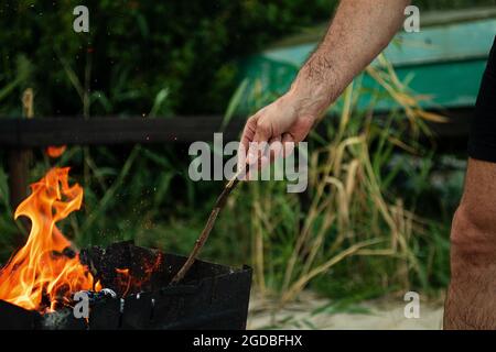 Un homme tient un bâton dans ses mains et allume le feu dans la nature.concept de pique-nique à l'extérieur. Banque D'Images