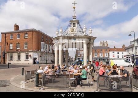 Scène de rue Beverley Yorkshire; personnes assises autour de la Croix du marché du XIXe siècle sur la place du marché, le centre-ville, Beverley Angleterre Royaume-Uni; Banque D'Images