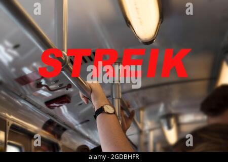 Texte allemand Streik (signifiant grève) et une main tenant sur le bar dans un train de métro pendant l'heure de pointe, focus sélectionné, profondeur de champ étroite Banque D'Images