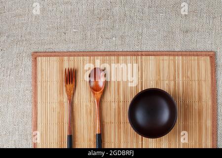 Assiette en bois naturel, cuillère et fourchette sur un support en bambou. Concept d'artisanat alimentaire asiatique. Vue de dessus Banque D'Images