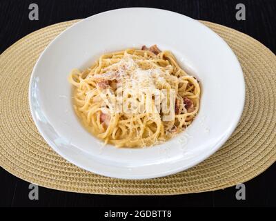 spaghetti alla carbonara en plaque blanche sur un tapis de paille sur une table en bois sombre Banque D'Images