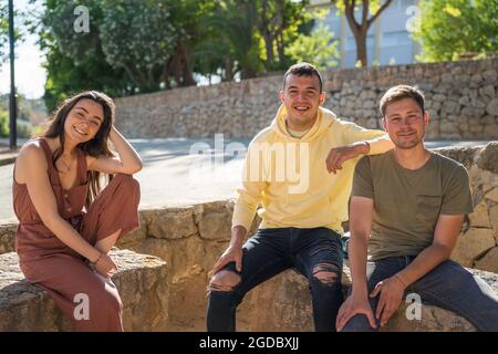 Groupe d'amis assis dans un parc. Ils regardent la caméra sourire. Ils sont blancs. Ils portent des vêtements d'été colorés. Ils sont ha Banque D'Images