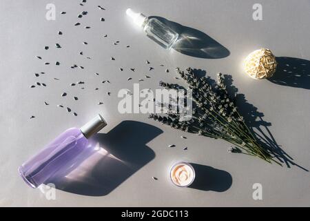 Fleurs de lavande et hydrolat, sérum en bouteilles de verre, pot crème sur fond gris clair, vue du dessus. Concept d'aromathérapie et de cosmétiques naturels. Plat Banque D'Images