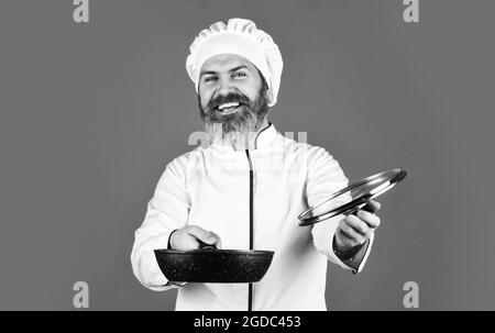 Poêle de haute qualité. Homme barbu cuisinier blanc uniforme. Petit-déjeuner maison. Cuisiner comme un pro. Repas savoureux et facile préparés à la maison. Récipient en céramique Banque D'Images