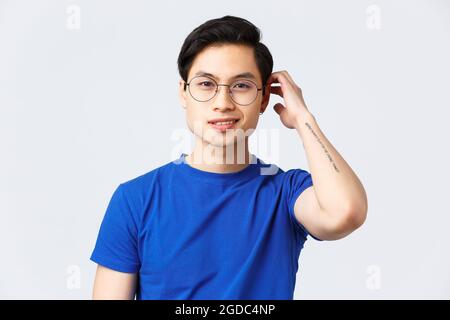 Style de vie, émotions et beauté des gens. Beau jeune homme asiatique confiant avec une nouvelle coupe de cheveux, se brosser les cheveux avec la main et sourire heureux comme Banque D'Images