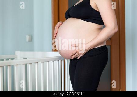Vue latérale sur le ventre de la femme caucasienne, femme debout près du lit d'enfants Banque D'Images