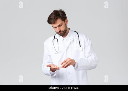 Hôpital, personnel de santé, concept de traitement Covid-19. Médecin sérieux-regardant dans les exfoliations blanches avec stéthoscope, les pilules de comptage, médicaments dans Banque D'Images