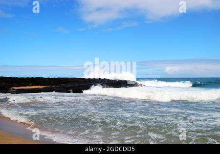 Les vagues se brisent contre un éperon rocheux de lave noire sur l'île de Kauai, Hawaï. Horizon et océan s'étendent vers le ciel bleu. Banque D'Images