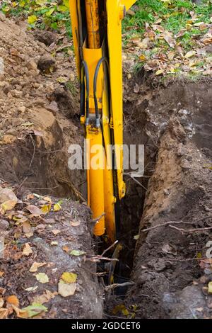 La pelle creuse un trou. Flèche jaune avec un seau dans le sol, préparant une tranchée pour un puits d'égout. Banque D'Images
